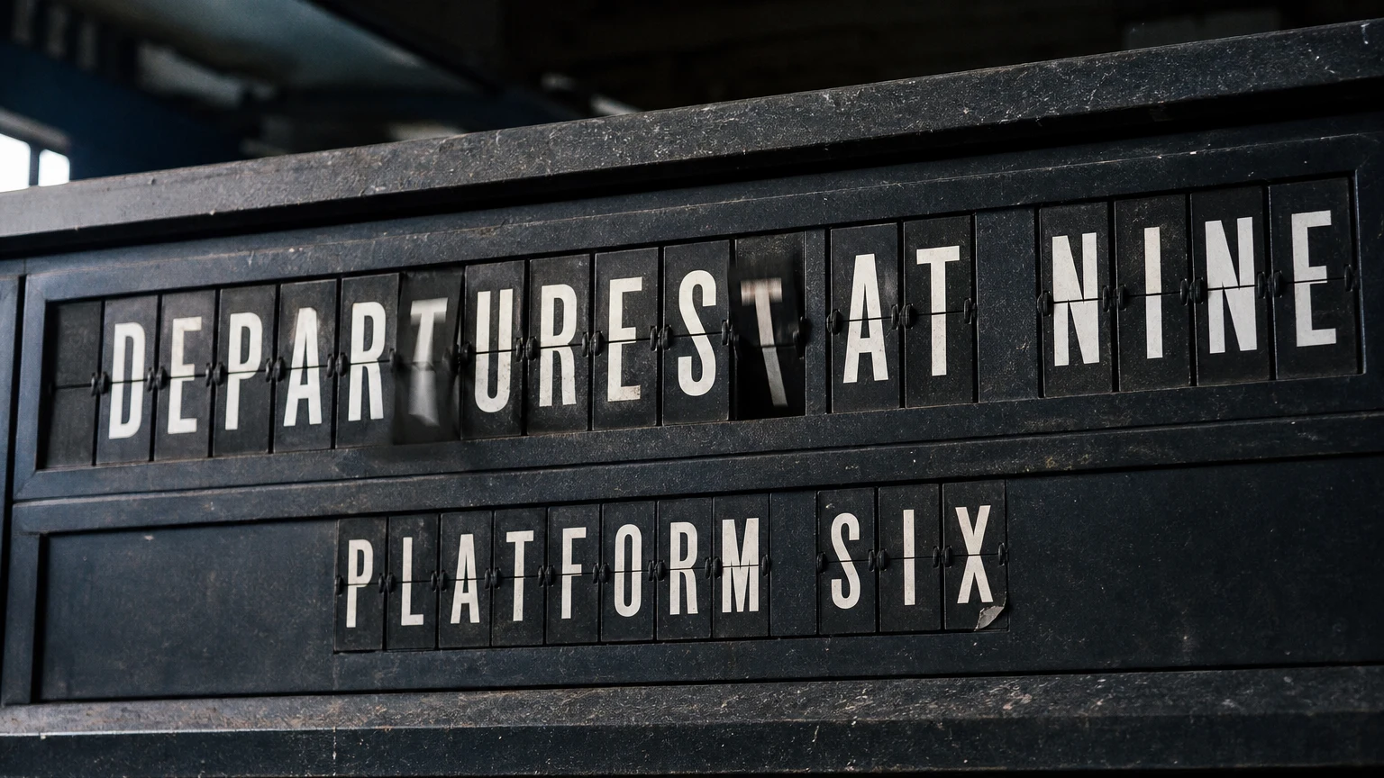 A mechanical split-flap board mid-flip spelling a title in worn white-on-black flap letters.